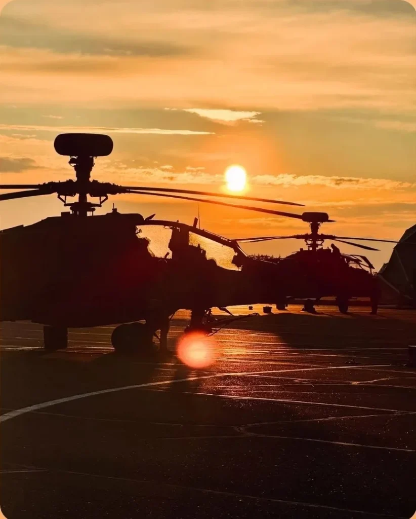 노을 속 비행장에 서 있는 AH-64 헬리콥터